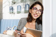 © Анна Демидова - Smiling young brunette woman in glasses with a tablet sits in a cafe and looks out the window. Online business and distance learning.