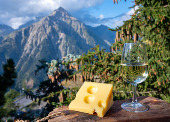 Glass of swiss or savoy dry white wine and yellow emmental cheese with Alpine mountains peaks on background