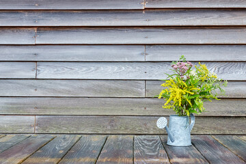 Wildflowers in a Watering Can on a Wooden Surface in Front of a Wooden Wall with Copyspace, Horizontal View 2