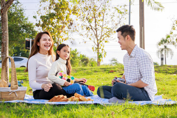 Happy family picnic. A little girl playing ukulele with her parents (Father, Mother) during picnicking on a picnic cloth on a sunny day. family relaxes in the green park. Family weekend