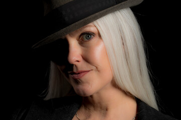 Wall Mural - Image of a beautiful mature woman with platinum blonde hair, wearing a hat. Studio image with a black background.