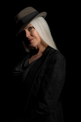 Wall Mural - Image of a beautiful mature woman with platinum blonde hair, wearing a hat. Studio image with a black background.