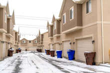 Apartments exterior with trash cans on the snowy road in front of garage doors