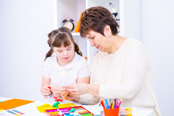 Wall Mural - The teacher shows the student with down syndrome how to do creativity. Girl with down syndrome smiles at teacher