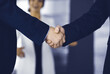 © cameravit - Unknown businesspeople are shaking their hands after signing a contract, while standing together in a modern office, close-up. Business communication, handshake, and marketing concept