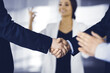 © cameravit - Businessmen are shaking hands while standing with colleagues applauding in office, close-up. Business success concept