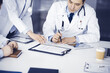 © cameravit - Group of unknown doctors are sitting at the desk and discussing medical treatment, using a clipboard, close-up. Team of physicians at work in a clinic. Medicine and healthcare concept