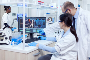 Wall Mural - Group of scientist working with computer in laboratory. Team of researchers doing pharmacology engineering in sterile lab for healthcare industry with african assistant in the background.