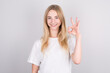 © Studio Nova - Girl with long, white hair smiling and showing ok sign on white background.