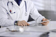 © rogerphoto - Unknown male doctor sitting and working with tablet computer in clinic at his working place, close-up. Young physician at work. Perfect medical service, medicine concept