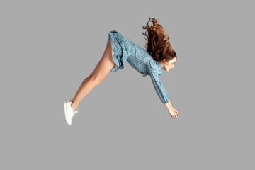 Wall Mural - Side view girl rushing at full speed accelerate, steering driving fast and levitating in air. Model flying rapidly with hurricane wind blowing extremely sharply. indoor studio shot isolated on gray