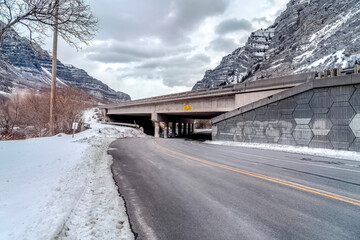 Canvas Print - Highway road passing under a bridge against rocky mountain and cloudy sky views