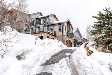 Canvas Print - Road going up a snowy slope leading to houses with cloudy sky overhead in winter