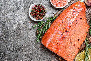 Fresh raw salmon fish fillet with cooking ingredients, herbs and lemon on gray concrete background. Healthy diet food