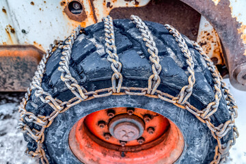 Wall Mural - Close up of the black wheel of a bulldozer with rusty chains on a snowy terrain