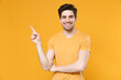 Young smiling unshaved caucasian handsome man 20s in casual blank print design t-shirt pointing finger aside on workspace copy space area mock up isolated on yellow color background studio portrait.