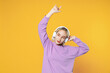 © ViDi Studio - Young blonde caucasian woman bob haircut makeup wearing basic purple shirt raised hands enjoy listen music in headphones touching earphones looking aside isolated on yellow background studio portrait.