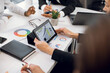 © sofiko14 - Close up cropped image of hands of diverse team of businesspeople, sitting at the table at office, and working with laptop, tablet i-pad and charts infographics. Business meeting concept