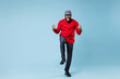 © ViDi Studio - Full length happy joyful young bearded african american man in casual red shirt cap eyeglasses standing doing winner gesture clenching fists isolated on pastel blue color background studio portrait.