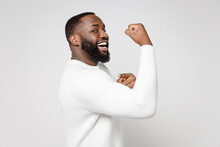 Side View Of Funny Strong Cheerful Young African American Man 20s Wearing Casual Basic Sweater Standing Showing Biceps Muscles Looking Camera Isolated On White Color Wall Background Studio Portrait.
