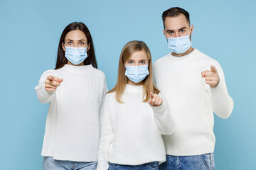 Wall Mural - Young parents mom dad with child kid daughter teen girl in sweaters sterile face mask safe from coronavirus virus covid-19 point fingers camera isolated on blue background. Family parenthood concept.