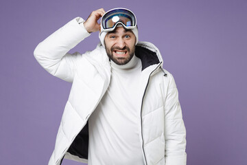 Wall Mural - Preoccupied skier man in warm white windbreaker jacket ski goggles mask put hand on head spend extreme weekend winter season in mountains isolated on purple background. People lifestyle hobby concept.