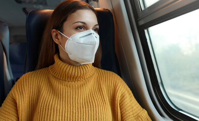 Travel safely. Young business woman with KN95 FFP2 face mask looking through train window. Train passenger with protective mask travels sitting in business class looking through the window.