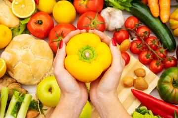 Close up of a cook holding a yellow pepper in her hands on a table with vegetables