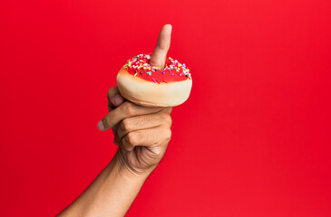 Wall Mural - Finger of hispanic man holding donut over isolated red background.