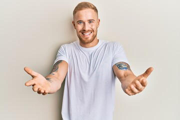 Young caucasian man wearing casual white tshirt looking at the camera smiling with open arms for hug. cheerful expression embracing happiness.