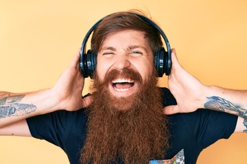 Canvas Print - Handsome young red head man with long beard listening to music using headphones smiling and laughing hard out loud because funny crazy joke.