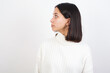 © Roquillo - Close up side profile photo Young brunette woman wearing white knitted sweater against white background not smiling attentive listen concentrated