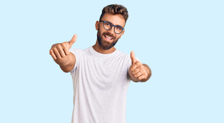 Young hispanic man wearing casual clothes and glasses approving doing positive gesture with hand, thumbs up smiling and happy for success. winner gesture.