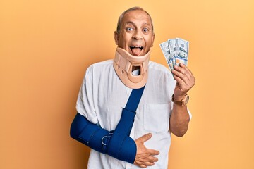 Poster - Handsome mature injured man wearing cervical collar and sling holding insurance money sticking tongue out happy with funny expression.