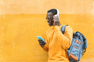 Wall Mural - Black Man Listening Music Using Cellphone Wearing Yellow Sweater Outdoors.