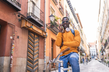 Wall Mural - Black Man Riding Bike Having Phone Call Wearing Yellow Sweater Outdoors.