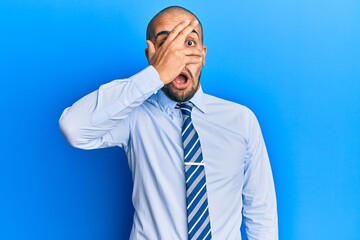 Wall Mural - Hispanic adult man wearing business shirt and tie peeking in shock covering face and eyes with hand, looking through fingers afraid