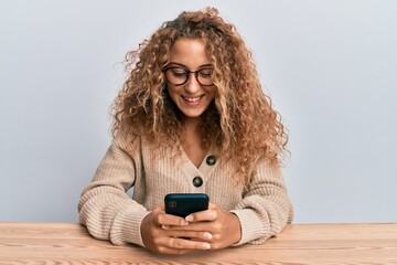 Poster - Beautiful caucasian teenager girl using smartphone sitting on the table winking looking at the camera with sexy expression, cheerful and happy face.