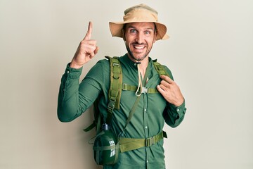 Sticker - Handsome man with beard wearing explorer hat and backpack smiling amazed and surprised and pointing up with fingers and raised arms.