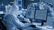 Electronics Factory Cleanroom: Engineer / Scientist in Coveralls Works on Computer, Screen Shows Infographics and Software System Control UI, Developing Electronics for Medical Electronics