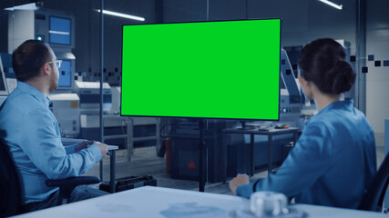 Wall Mural - Office Meeting: Confident Female Engineer Talks to Project Manager, Watching Interactive Digital Whiteboard TV that Shows Green Screen Chroma Key Display. Modern Factory with Machinery