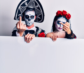 Canvas Print - Young couple wearing mexican day of the dead costume holding blank empty banner showing middle finger, impolite and rude fuck off expression