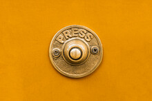 Vintage Style Solid Golden Brass Metal Doorbell Button Against A Seamless Bright Yellow Painted Wall.