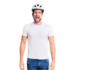 Wall Mural - Young handsome man wearing bike helmet sticking tongue out happy with funny expression. emotion concept.