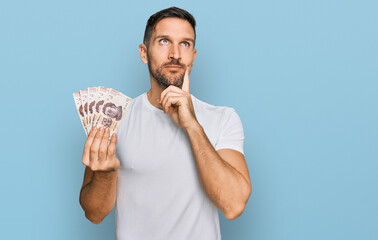 Sticker - Handsome man with beard holding 50 mexican pesos banknotes serious face thinking about question with hand on chin, thoughtful about confusing idea