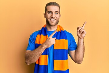 Poster - Young caucasian man football hooligan cheering game smiling and looking at the camera pointing with two hands and fingers to the side.