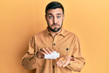 Canvas Print - Young hispanic man holding pills puffing cheeks with funny face. mouth inflated with air, catching air.