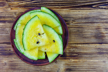 Wall Mural - Plate with sliced yellow watermelon on a wooden table. Top view