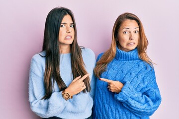 Poster - Hispanic family of mother and daughter wearing wool winter sweater pointing aside worried and nervous with forefinger, concerned and surprised expression