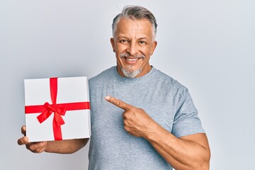 Wall Mural - Middle age grey-haired man holding gift smiling happy pointing with hand and finger